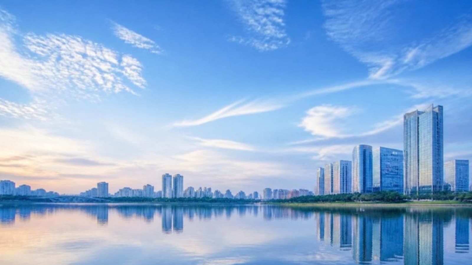 A city skyline reflected in still water under a blue sky